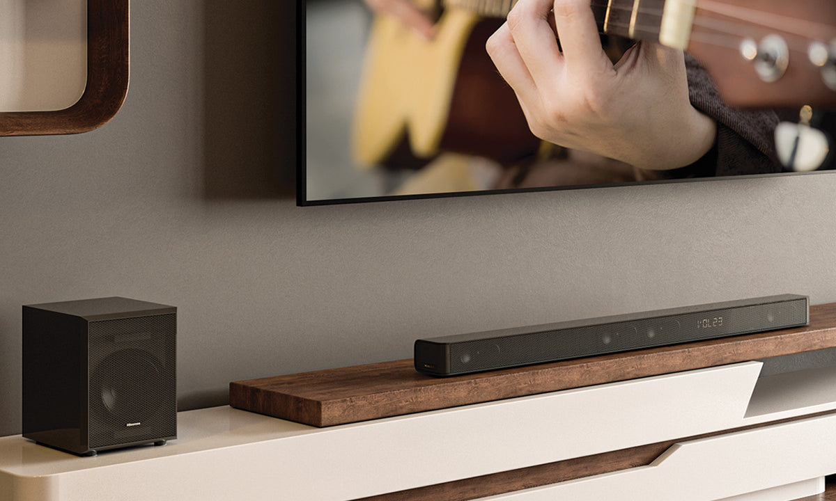 A Hisense soundbar and Subwoofer sitting on a piece of wood on a tv cabinet with a TV featured above it