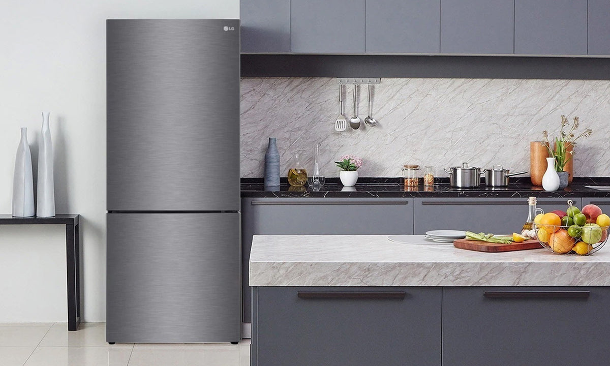A LG Bottom Mount Fridge in stainless steel in a slate gray kitchen with assorted vibrant fruits on the marble countertops