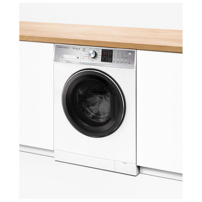 Angle view of the Fisher & Paykel 9kg front load washing machine in a white finish, showing the machine washing a load in a modern laundry setting, with white cabinetry besides it and a wooden benchtop above it.