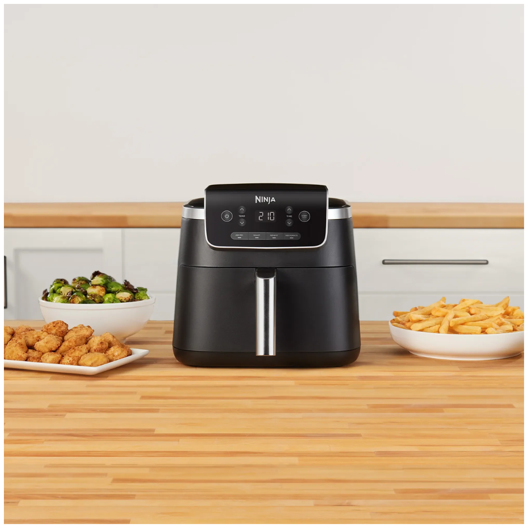 Ninja air fryer on a wooden kitchen counter with food items around