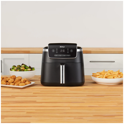 Ninja air fryer on a wooden kitchen counter with food items around