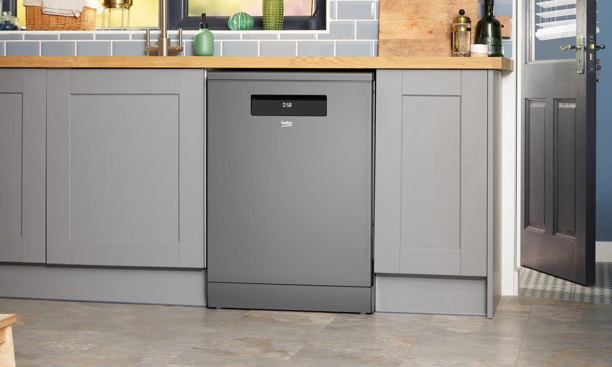 A beko dishwasher in matte stainless steel in a gray kitchen with a wooden counter top and a dark blue door leading outside