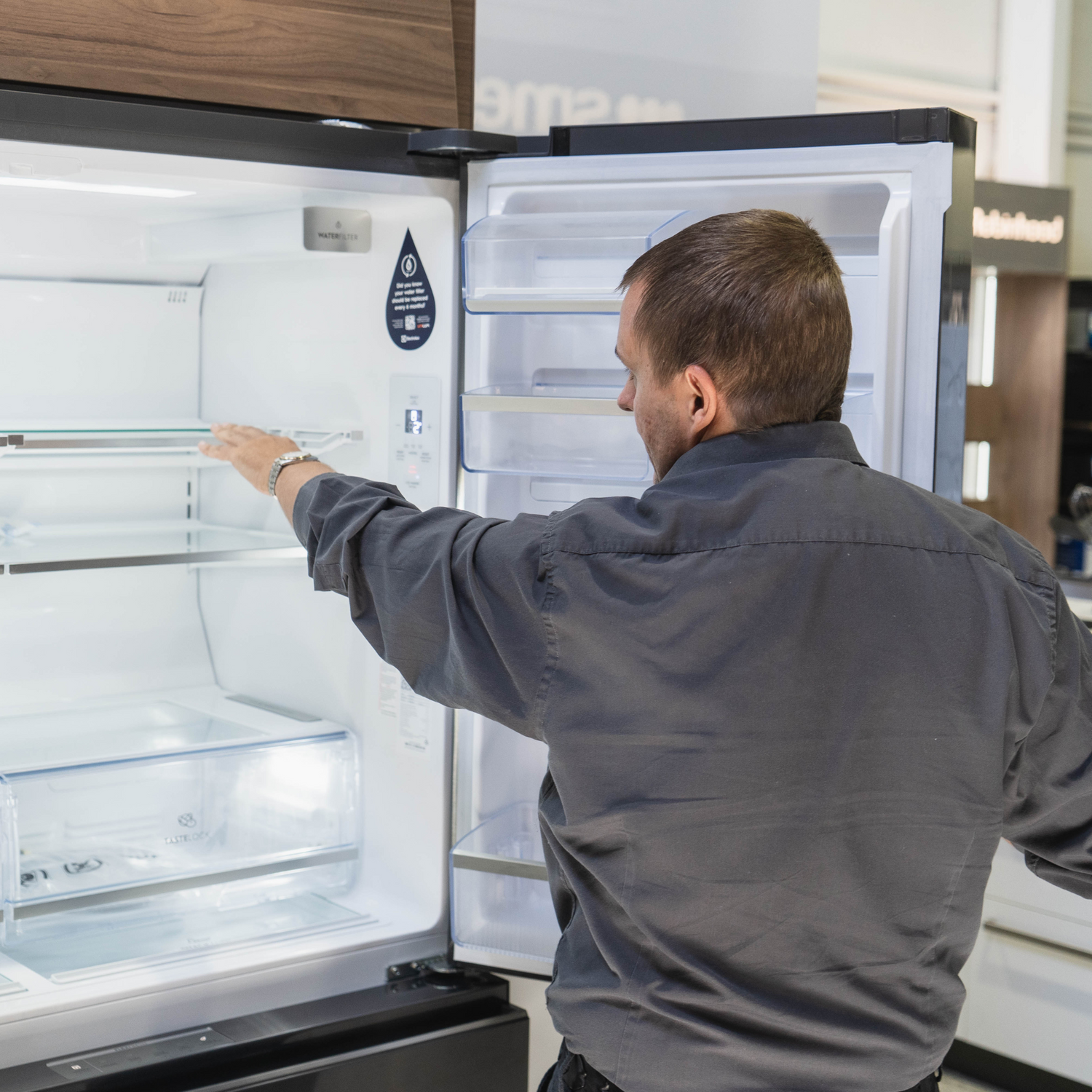 image of a man gesturing inside a fridge, he's wearing a charcoal coloured shirt with a collar and long sleeves