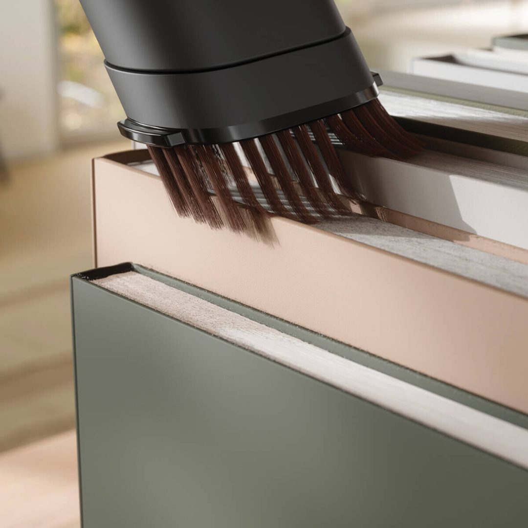 Close up view of the Electrolux 600 series cordless stick vacuum with the dust brush attachment being used to clean the top of some books on a shelf.