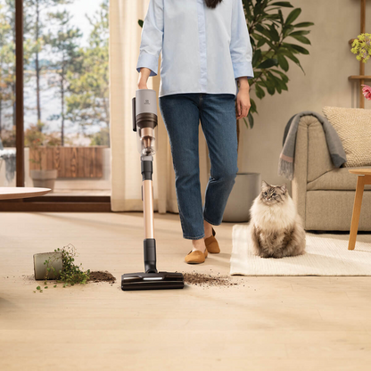 Person using an Electrolux 800 series cordless stick vacuum with PetPro nozzle to clean spilled soil near a cat in a bright living room, showing powerful suction and pet friendly design. 