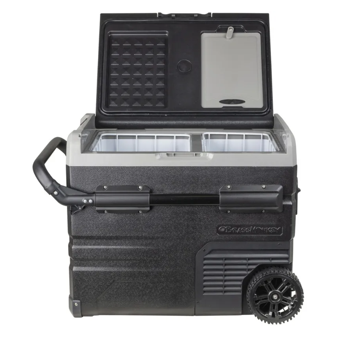 Brass Monkey dual zone portable fridge freezer with lid open showing two storage baskets and built-in chopping board, rugged wheels and extendable handle for outdoor camping or travel use.