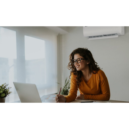 Woman sitting at a desk with a laptop, holding a pen and smiling with a Hisense Air Conditioner in the background. 