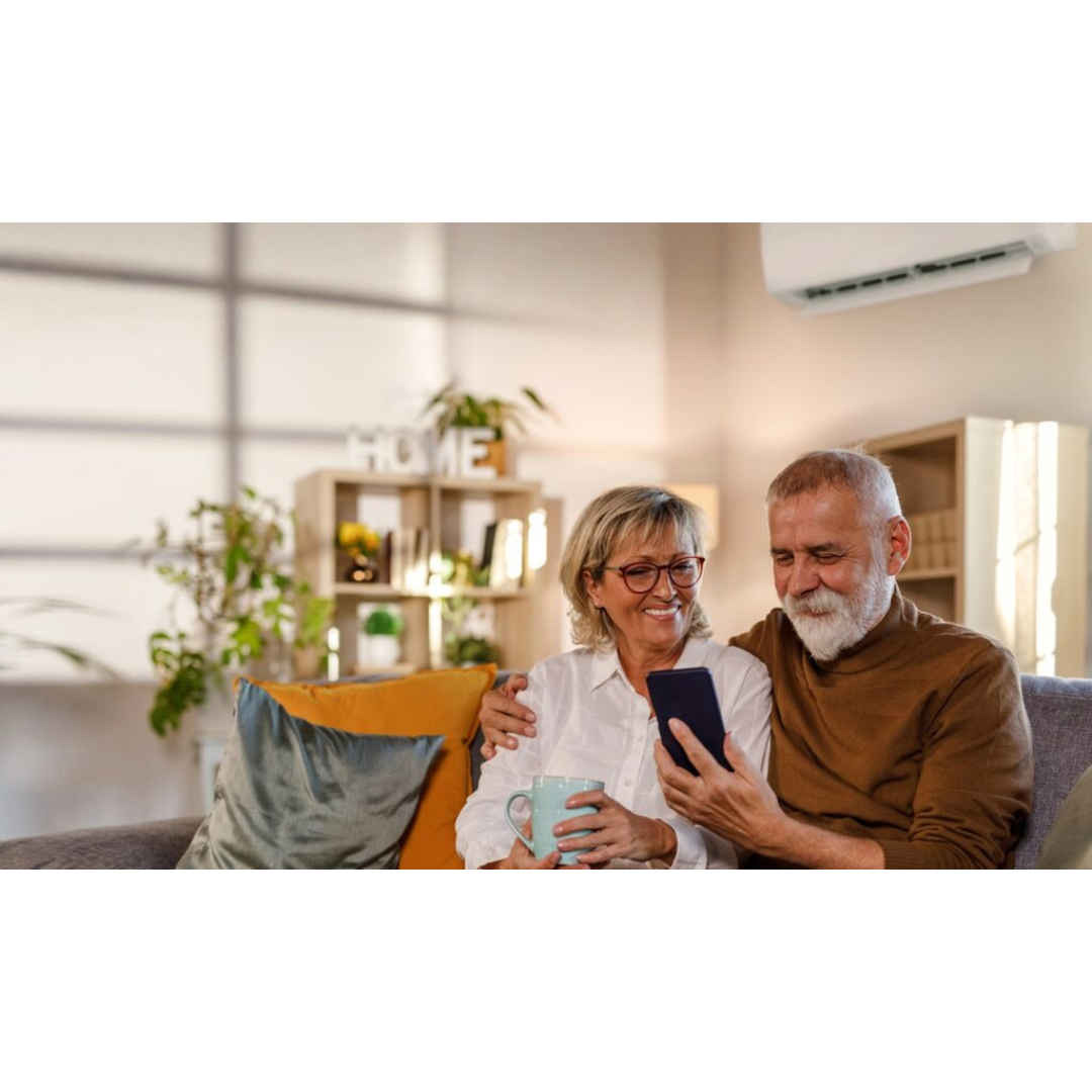 Senior couple sitting on a couch in a living room, using a smartphone together with a Hisense Air Conditioner in the background. 