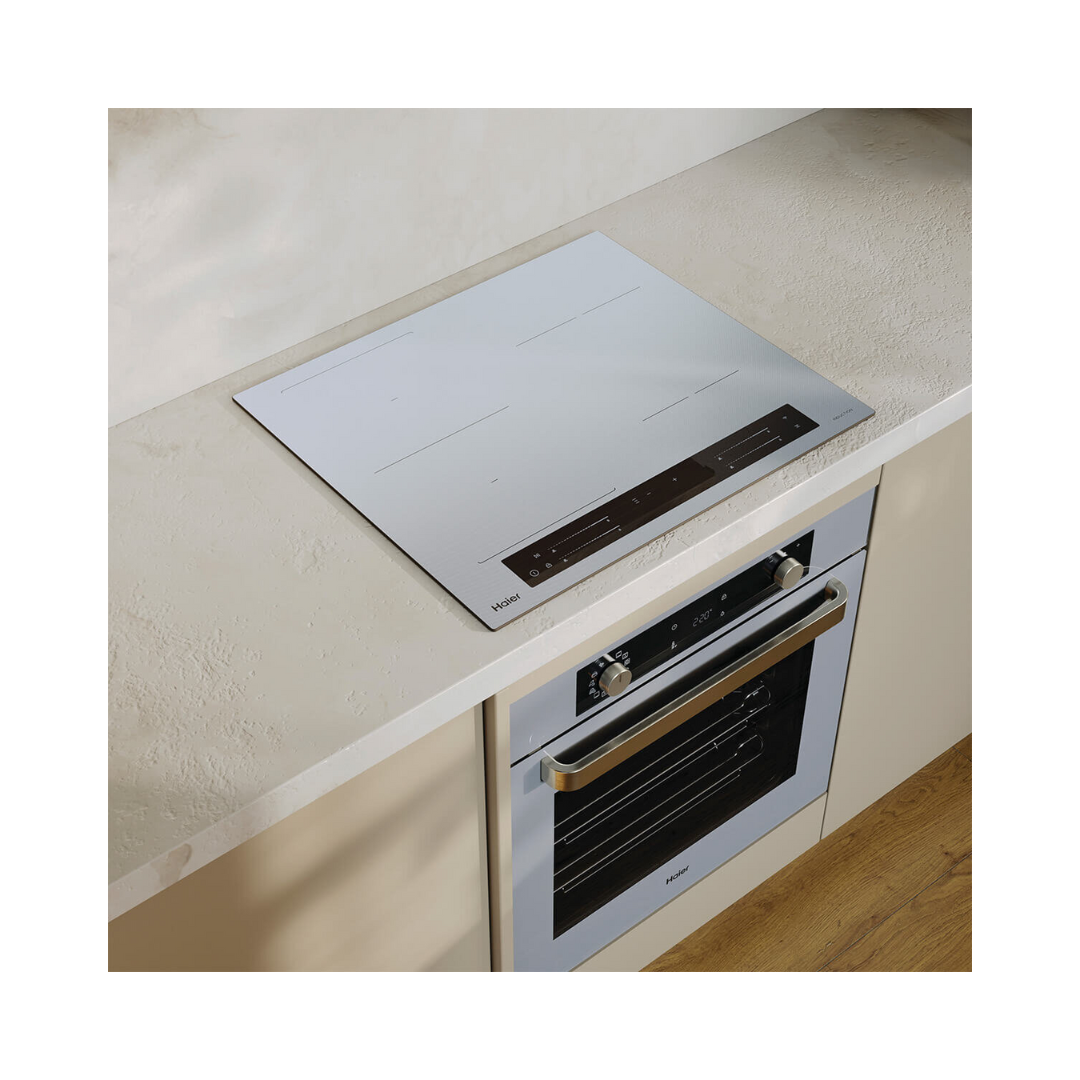 Angled image of the Haier induction cooktop and oven in a modern kitchen setting in a grey colourway. 