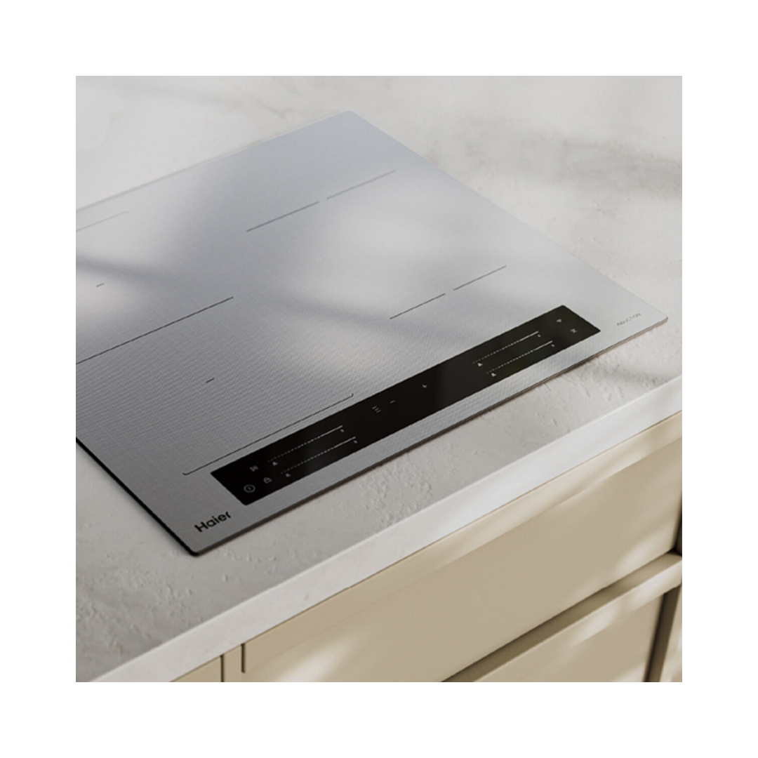 Angle image of the Haier induction cooktop in grey in a modern kitchen setting installed on a white benchtop. 