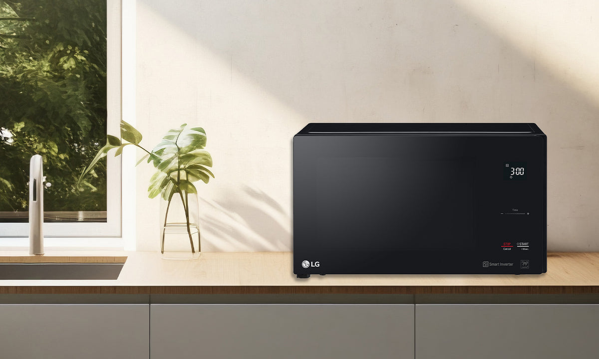 Black LG Microwave sitting on a kitchen counter beside a pot plant, sink and open window