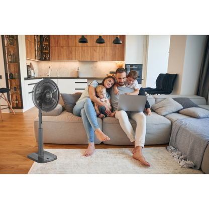 Family sitting on a couch with a laptop next to a standing fan in a living room showcasing the Mitsubishi Electric pedestal fan.