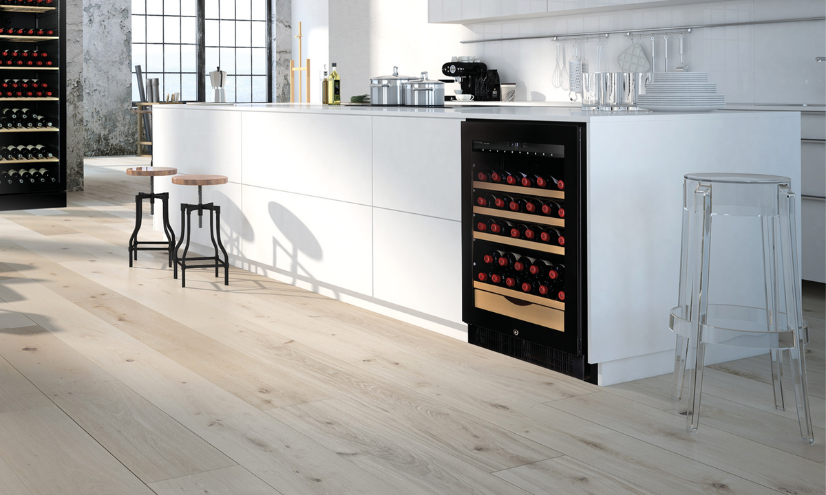 A white kitchen island with white wooden floors contrasts to the Vintec black Wine Cabinet in the island. 