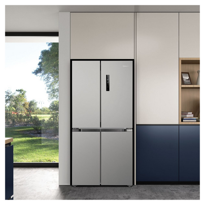 Front view of a 496L French Door Fridge with all doors closed in a modern kitchen setting with wooden cabinetry and open shelving. A picture frame and books are neatly arranged nearby. Natural light streaming though the window. 