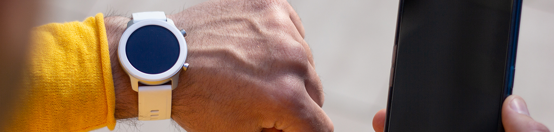 In this close-up image a white smartwatch with a white strap and circular watch face, and a black smartphone screen partially visible next to the smartwatch.